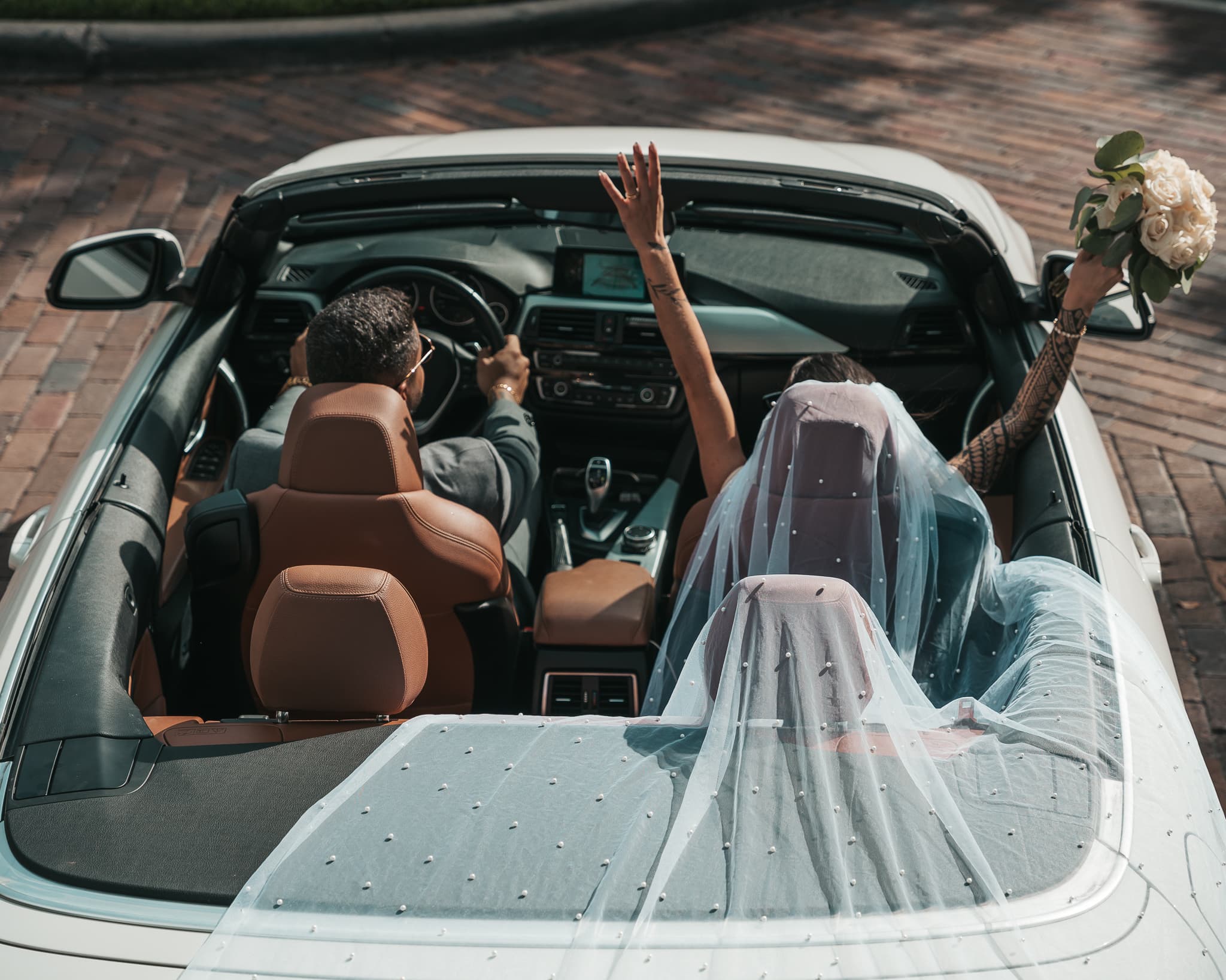 Newlyweds in convertible, veil flowing